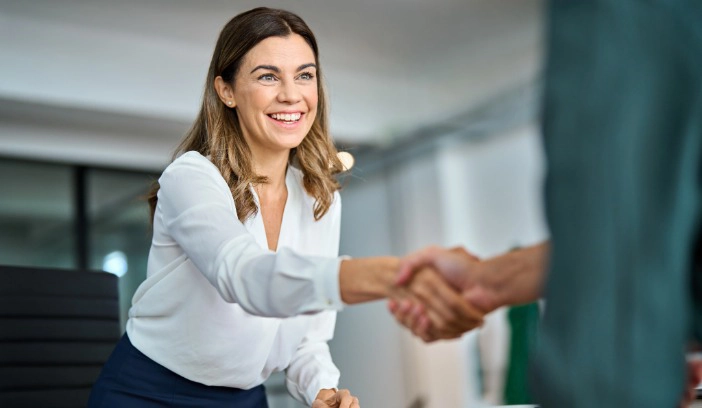 Eine Frau in weißer Bluse gibt jemanden die Hand auf Ihre neue Stelle als Personaldisponentin bei Flexiholding.